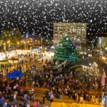 An aerial view of Alex Winter Fête bustling with crowds exploring food and art/retail vendors. Illuminated vendor booths surround a decorated central Christmas tree, while festival attendees enjoy food stalls, holiday-themed activities, and an ice skating rink under twinkling lights and falling snow.